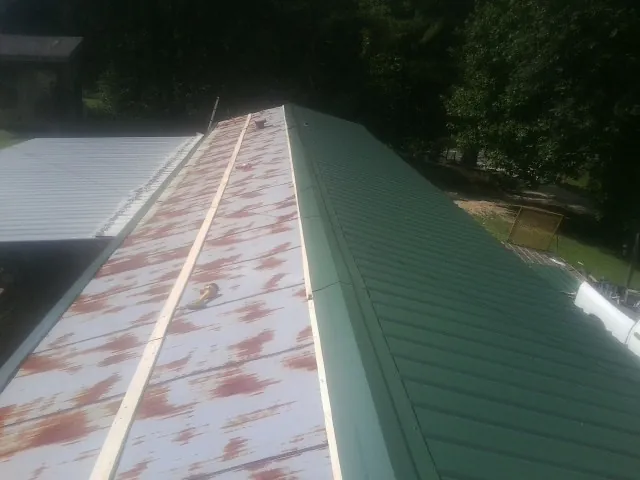 Old rusted panels beside newly installed green metal roofing — Wind Damage Roof Repair by Roofing Brothers in Refton