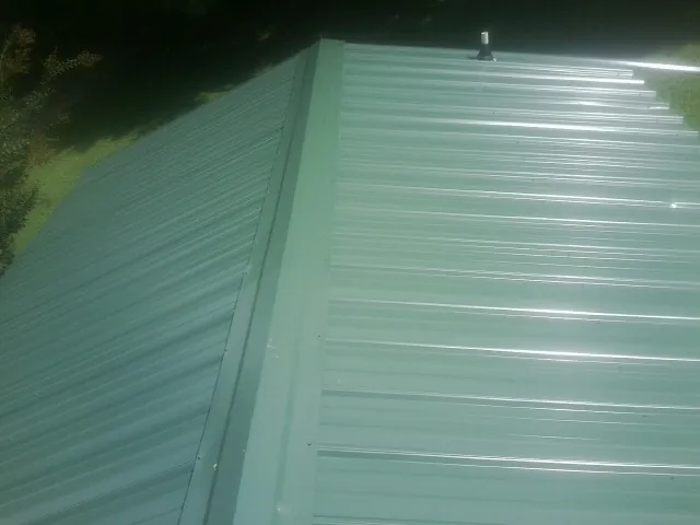 New green metal panels meeting at the ridge of a roof — Flat Roof Repair work by our crew in Refton