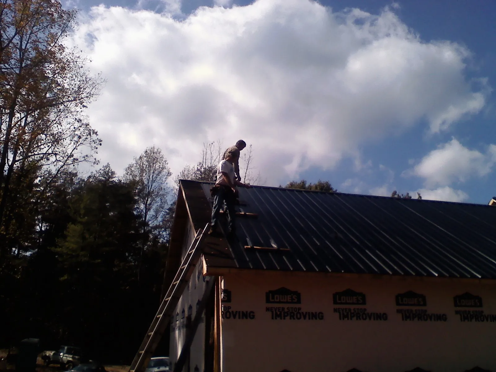 Roofer fastening dark metal panels high against a cloudy sky, from a Roof Inspection job in Refton