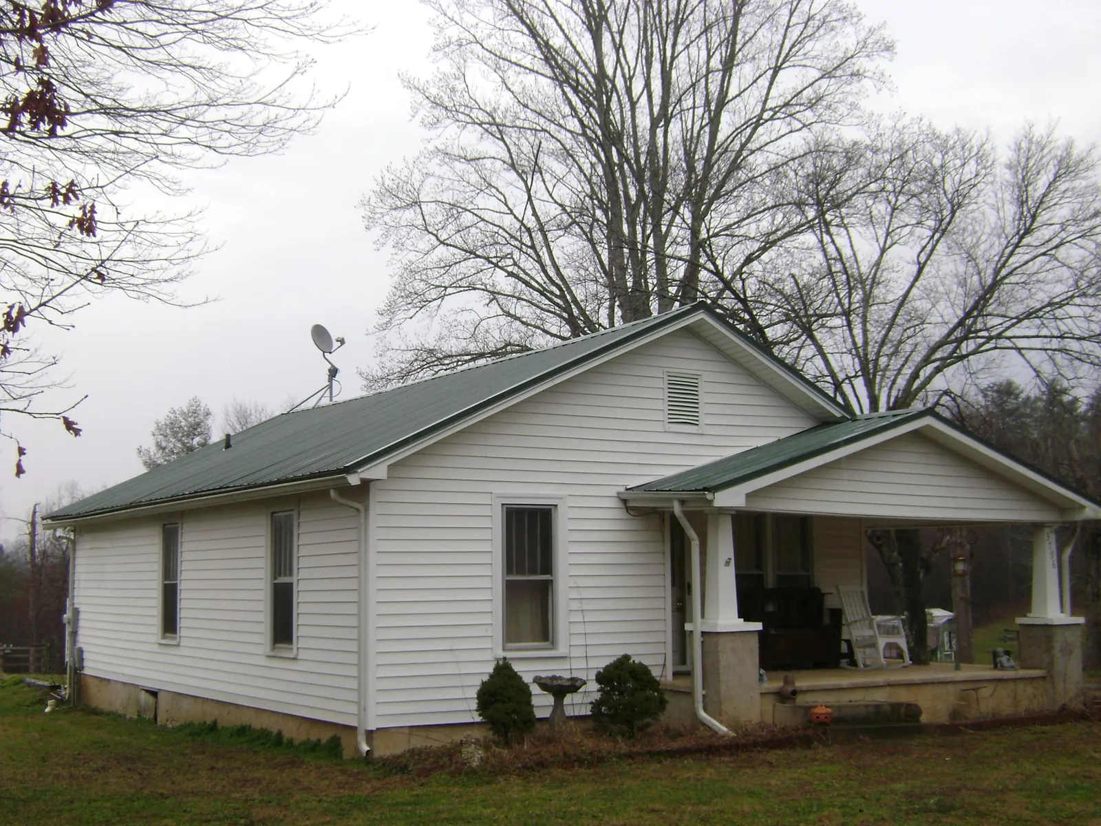 Green metal roof on a white bungalow with a side porch in Refton