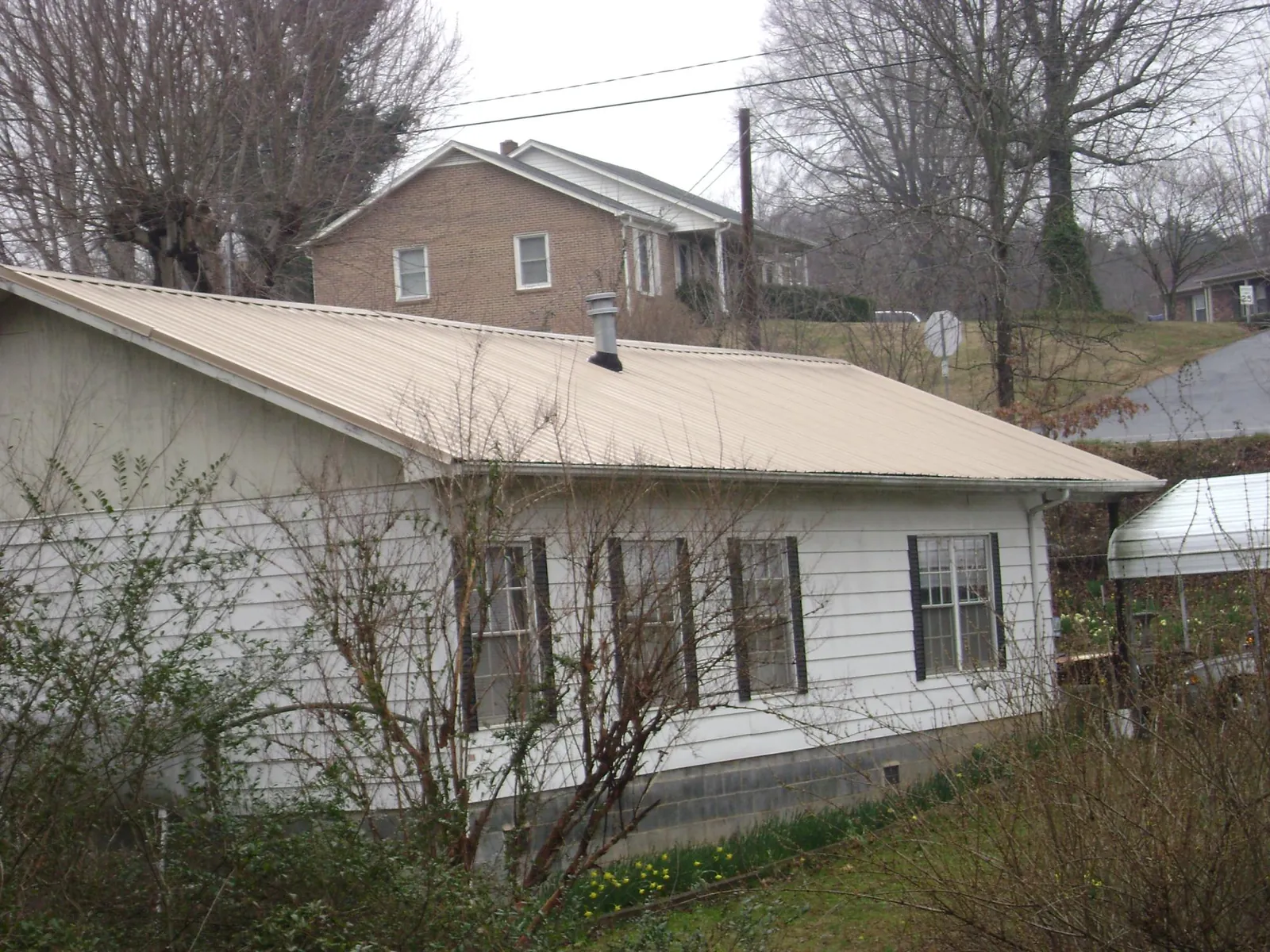 Tan metal roof on a white sided house set into a hillside — Commercial Roofing by Roofing Brothers in Refton